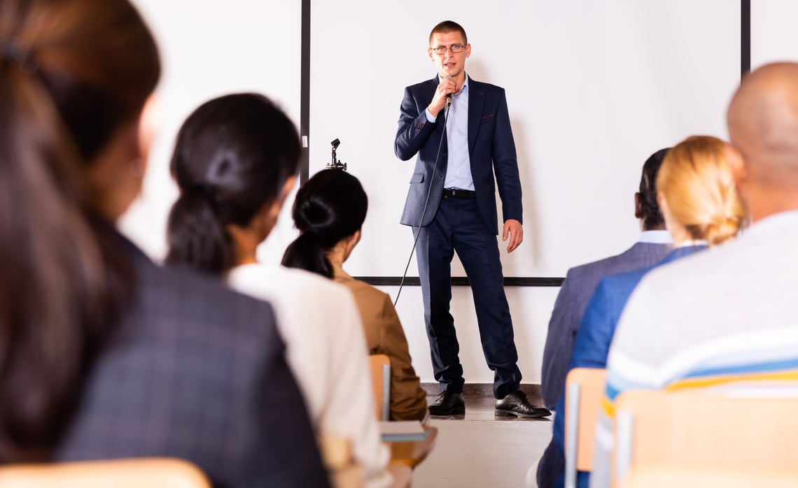 Business coach speaking from stage to audience at corporate training